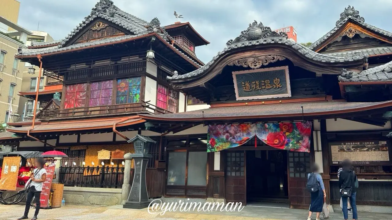 昼間の道後温泉本館に映る蜷川実花 with EiMの花のアート。日の光で淡く見えるが館内からは鮮やかに映える1