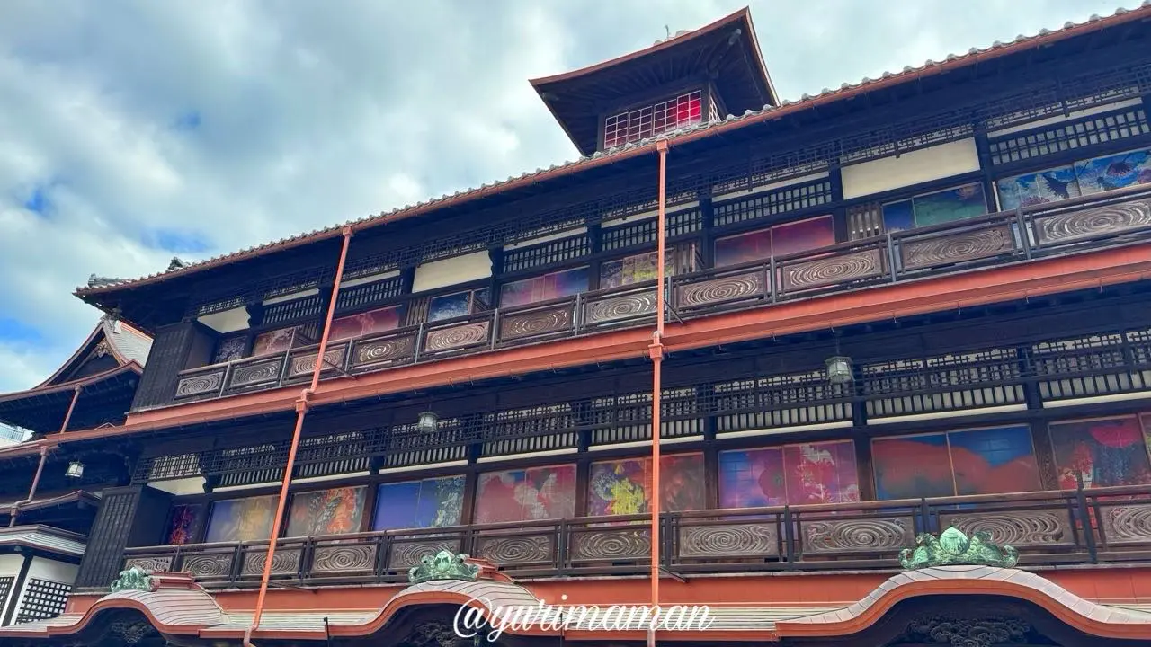 昼間の道後温泉本館に映る蜷川実花 with EiMの花のアート。日の光で淡く見えるが館内からは鮮やかに映える2