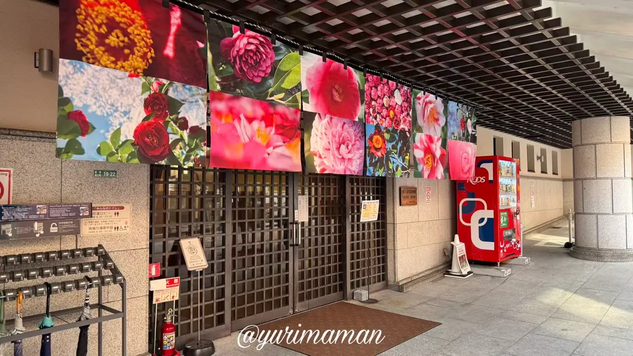 椿の湯入口に飾られた蜷川実花 with EiMの花アートのれん。日中の光に映えて華やか