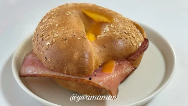 スターバックスのベーコンエッグチーズベーグルサンドをお皿にのせた実食写真。チーズがとろけて美味しそう。