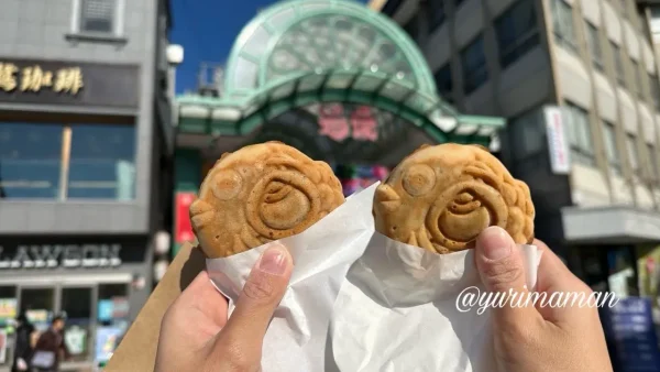 道後商店街を背景に、湯げの屋のたい焼きを手に持って食べ歩きしている様子。