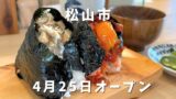 Rice balls wrapped in seaweed on a wooden board, with Japanese text announcing Matsuyama City and an April 25 opening.