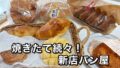 Assorted freshly baked breads in baskets and bags on a table, with bold Japanese text advertising a new bakery.
