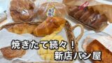 Assorted freshly baked breads in baskets and bags on a table, with bold Japanese text advertising a new bakery.