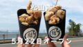 Two black cups of fried chicken being held up outdoors with a seaside road in the background; white Japanese text reads 松山市 and 5月22日オープン (Matsuyama City May 22 opening).