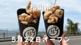 松山市北条の海を背景に撮影した唐揚げ専門店「結び」の唐揚げテイクアウト写真 - ゆりママんブログ Two black cups of fried chicken being held up outdoors with a seaside road in the background; white Japanese text reads 松山市 and 5月22日オープン (Matsuyama City May 22 opening).