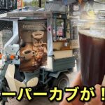 Teal motorized coffee cart on a small scooter, with a Dripped Coffee poster and a large iced coffee cup in the foreground; street setting.