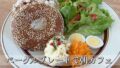 sesame seed bagel with cream cheese, greens, potato salad, shredded carrot and two deviled eggs on a white plate