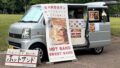 Mobile sandwich van with a large banner advertising HOT SAND and SWEET SAND, and a sandwich-board sign in front displaying the menu