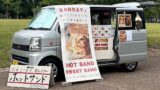 Mobile sandwich van with a large banner advertising HOT SAND and SWEET SAND, and a sandwich-board sign in front displaying the menu