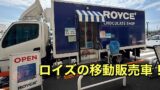 Blue Royce Chocolate Shop mobile truck with striped awning and an OPEN sign outside a crosswalk area.