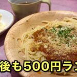 Spaghetti with meat sauce and grated cheese on a wooden plate, with a side salad and a mug nearby; bold Japanese text promoting a 500 yen lunch.