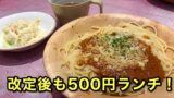 Spaghetti with meat sauce and grated cheese on a wooden plate, with a side salad and a mug nearby; bold Japanese text promoting a 500 yen lunch.