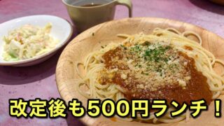 Spaghetti with meat sauce and grated cheese on a wooden plate, with a side salad and a mug nearby; bold Japanese text promoting a 500 yen lunch.