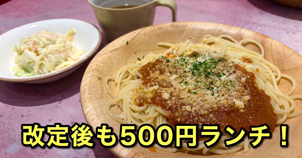 Spaghetti with meat sauce and grated cheese on a wooden plate, with a side salad and a mug nearby; bold Japanese text promoting a 500 yen lunch.