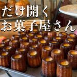 Text in Japanese reads '週一だけ開くお菓子屋さん' over a display of canelé pastries on a tray with pumpkins and fruit in the background.