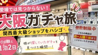 Bright Japanese promo banner for an Osaka gacha trip in a shop, with large pink kanji text and colorful banners in front of gachapon machines.