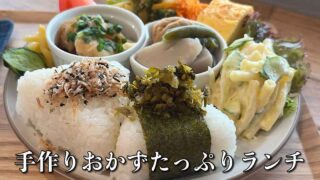 Plate with two onigiri and assorted side dishes (pickles, pasta salad, vegetables); caption: 手作りおかずたっぷりランチ.