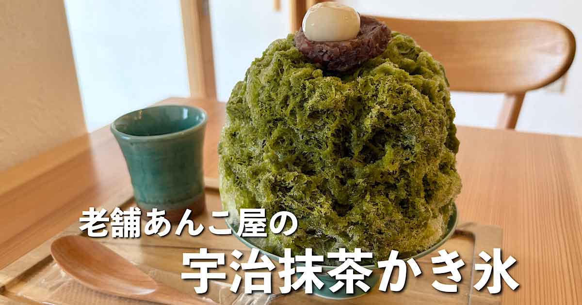 Large bowl of green matcha shaved ice topped with red bean paste and a white mochi on top, on a wooden table